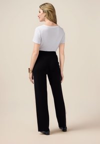Haut blanc à manches courtes associé à un pantalon noir taille haute. Les pantalons ont un design à jambe large et une texture lisse. Look minimaliste.