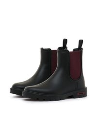 Stivali alla caviglia in gomma nera con pannelli elastici bordeaux ai lati, dotati di linguette per un facile indossamento e suola con grip strutturato.