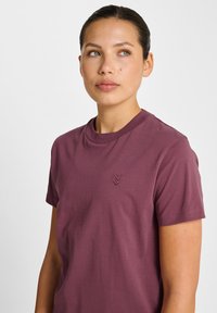 Bordowa koszulka z krótkim rękawem i okrągłym dekoltem, z małym haftowanym wzorem w kształcie szewrona na piersi. Wykonana z miękkiej bawełny.