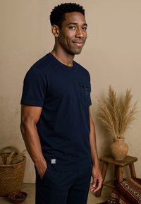 Donkerblauwe katoenen t-shirt met een frontzak met rits, ronde hals en korte mouwen, gecombineerd met donkere broek.