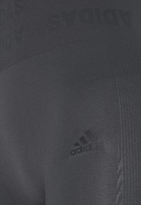 Granatowe legginsy sportowe wykonane z elastycznego materiału, z wytłaczanym logo adidas i teksturowanymi panelami dla dodatkowego stylu.