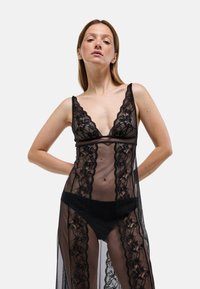 Nuisette en dentelle noire avec un décolleté plongeant en V, des motifs floraux délicats, un tissu transparent et des bretelles ajustables, accompagnée d'un string noir en dessous.