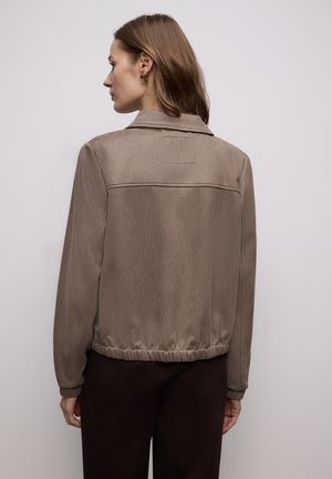 Brązowa kurtka o fakturowanej powierzchni, z kołnierzem i elastycznym paskiem w talii. Posiada prosty tył z małą wszywaną metką.