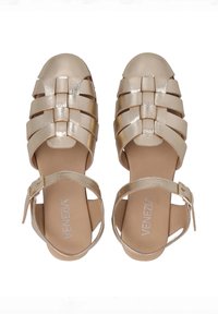 Metallisch goldene Sandalen mit geflochtenem Design, offenen Zehen und Knöchelriemen mit einer Schnalle. Glattes Lederoberteil mit flacher Sohle.