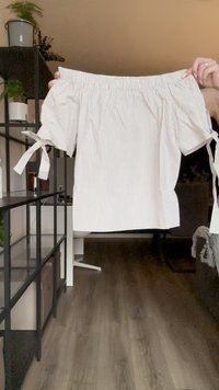 Off-the-shoulder blouse in white with narrow blue stripes. Features elastic neckline, short sleeves with ties, and a straight hem.