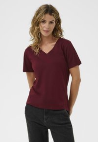 Burgundy v-neck t-shirt with short sleeves, made of soft fabric. Simple design without patterns or accents. Paired with dark jeans.