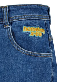 Tamsiai mėlynos džinsinės kelnės su kontrastingomis oranžinėmis siūlėmis. Yra užpakalinis kišenė, ant kurios išsiuvinėta "homeboy X-tra" ryškiai geltonos ir mėlynos spalvos.