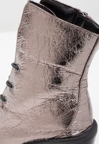 Bottine métallique à texture craquelée avec lacets et semelle noirs, dotée d'une surface brillante et réfléchissante.