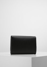 Clutch in pelle nera con una texture liscia, forma rettangolare, design pieghevole e bordi puliti, appoggiato su un pedestal bianco.