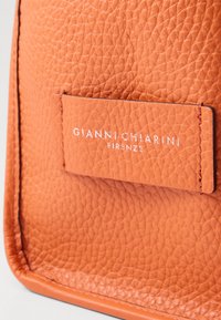 Borsa a tracolla in pelle arancione con una texture, dotata di un'etichetta logo argentata che riporta la scritta "GIANNI CHIARINI FIRENZE" cucita sulla parte anteriore.