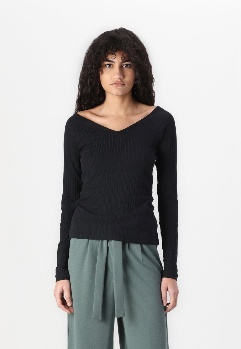 Black ribbed long-sleeve top with a V-neck design, paired with high-waisted green trousers featuring a tied waistband.
