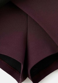 Primo piano di un tessuto piegato di colore viola scuro con texture visibile e bordi cuciti, su sfondo bianco.