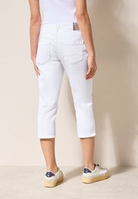 Un pantalon court blanc à coupe slim, avec deux poches arrière, des détails cousus et une étiquette à la taille. Associé à des baskets blanches.