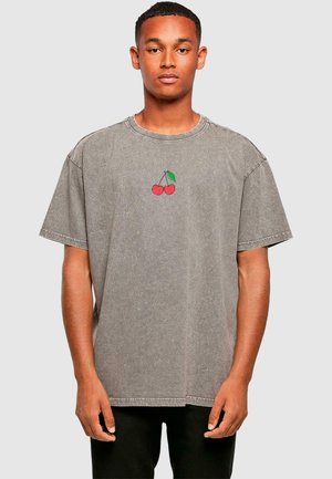 Grijze, oversized katoenen t-shirt met een kleine rode kers afbeelding met een groen blad op de borst. Korte mouwen en een ontspannen pasvorm.