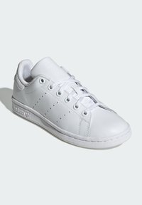 Λευκό δερμάτινο αθλητικό παπούτσι με στρογγυλή μύτη, σχέδιο με λαστιχάκι, τρυπητά πλαϊνά χαρακτηριστικά και υφασμάτινη σόλα με υφή που φέρει το λογότυπο της μάρκας στο πλάι.