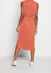 Hihaton, ruosteenvärinen midi-mekko, jossa on joustava vyötärö ja sivuaukot, valmistettu pehmeästä kankaasta, yhdistettynä valkoisiin tennareihin.