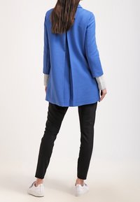 Blue textured jacket with a vertical seam, gray striped cuffs, paired with black slim-fit pants and white sneakers. Back view showcased.