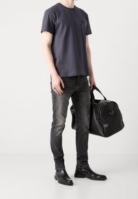 Černá kožená sportovní taška, šedé bavlněné tričko, oprané šedé džíny a černé kotníkové boty, tričko s malým logem.