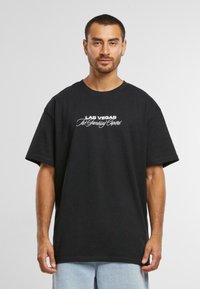 Sort oversized bomulds t-shirt med hvid tekst, der står "LAS VEGAS The Gambling Capital" henover brystet. Korte ærmer, rund hals design.
