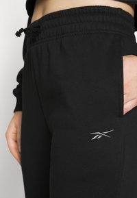 Svarta sweatpants med elastisk midja och snörning; har en sidoficka och en liten vit logotyp på vänster ben.