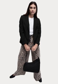 Černé zúžené sako přes bílé tričko, spárované s béžovými kalhotami s leopardím potiskem a širokým střihem. Černá texturovaná kabelka a elegantní černé boty.