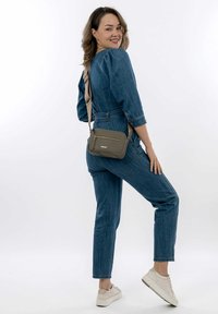 Une salopette en denim avec des manches bouffantes, de couleur bleue, et une taille cintrée. Associée à un sac bandoulière vert avec une poche zippée à l'avant. Des baskets décontractées.