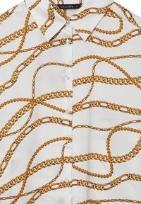 Weißes Hemd mit Button-Up, das ein Kettenmuster in Gold und Braun aufweist, mit runden Perlenknöpfen und einem klassischen Kragen.