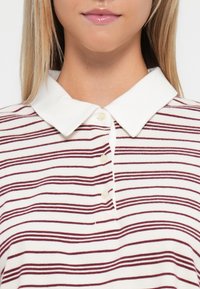 Polo en coton avec un col blanc, featuring des rayures horizontales bordeaux. Patte de boutonnage à cinq boutons et texture douce.