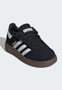 Svart semsket sneakers med tre hvite striper, snøring og brun gummisåle. Pyntet med gull "Spezial" logo.