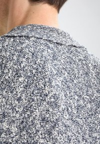 Polo shirt lavorato a maglia con motivo testurizzato in blu navy e bianco, dotato di un colletto morbido e dettagli di cucitura visibili.