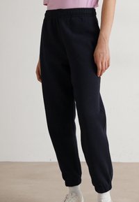 Mörkblå mjukisbyxor med elastisk midja, smalnande mudd och en mjuk textur. Bärs med en ljusrosa topp och vita sneakers.