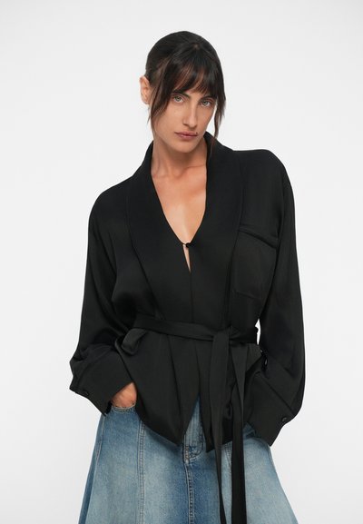 Black wrap blouse in smooth fabric, featuring a deep V-neck, long sleeves, and a tie belt. Includes a chest pocket with a flap.