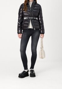 Svart vadderad jacka med dragkedja, elastiska ärmslut och ett bälte med varumärke. Kombinerad med mörka jeans och svarta platåskor. Texturerad svart handväska.