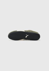 Sneaker underside with a textured black rubber sole, featuring a distinctive tread pattern and green suede upper with cream accents.