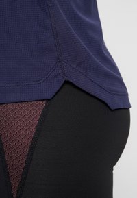 Top sportivo blu navy con trama, orlo curvo, abbinato a leggings neri con pannello in rete a diamante color marrone scuro sul lato.