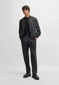 Veste bomber gris foncé avec col en côtes, associée à un pantalon tailleur assorti et des chaussures noires à lacets. Design simple et épuré.