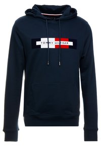 Granatowa bluza z kapturem z kieszenią typu kangur, sznurkami do regulacji oraz prostokątnym logo marki w kolorze czerwonym, białym i granatowym na klatce piersiowej. Miękka tekstura.