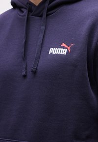 Μπλε σκουρό χούφτερ με κορδόνια, διακοσμημένο με μικρό κόκκινο λογότυπο Puma και λευκό κείμενο «PUMA» στο πάνω μέρος του στήθους.