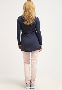 Námořnický dlouhý rukáv, upnutý v pase, v kombinaci se světlými růžovými kalhotami. Obuv jsou šedé tenisky. Hladká textura, jednoduchý design, bez viditelných vzorů.