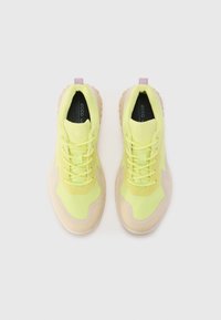 Limegröna sportskor med meshmaterial, beige gummisulor och kontrasterande snörning. Har en dragflik bak och texturerade detaljer.