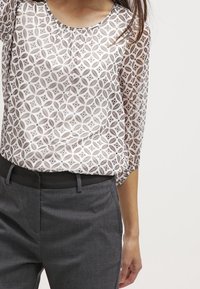 Blusa leggera e trasparente con un motivo geometrico in un morbido beige e marrone, completata da maniche a tre quarti ampie.