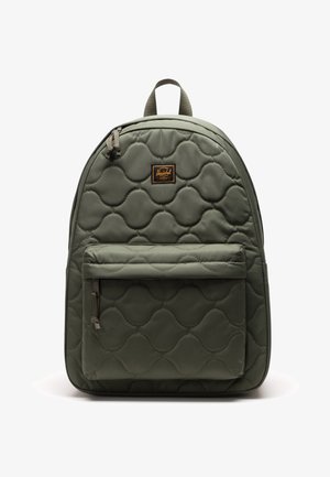 Zelený prešívaný batoh s prednou zipsovou kapsou, vystúpeným vlnitým vzorom a látkovou nášivkou loga. Obsahuje polstrované popruhy a hornú rukoväť.