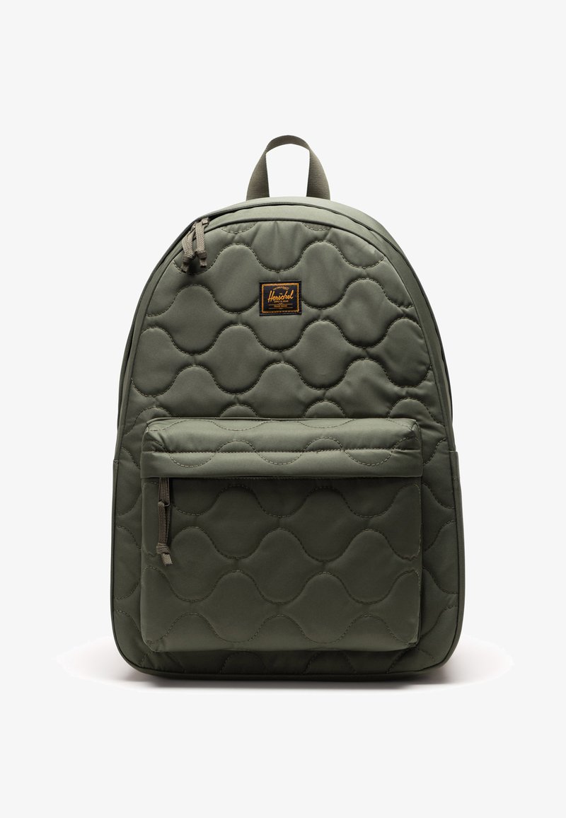 Zeleni kviltani ruksak s prednim zip džepom, uzdignutim valovitim uzorkom i oznakom od tkanine. Ima podstavljene naramenice i ručku na vrhu.