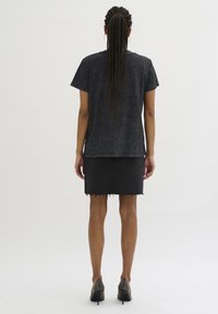 Top nero a maniche corte con vestibilità comoda, abbinato a una gonna di jeans scuri con orlo sfrangiato e scarpe con tacco alto con dettagli texture.
