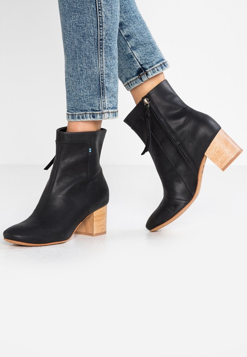 Bottes cheville en cuir noir avec un talon carré en bois, une fermeture éclair latérale et un bout arrondi. Un jean à ourlet effiloché complète cette tenue.