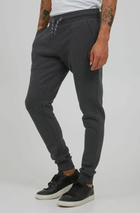 Los pantalones de chándal gris oscuro cuentan con una cintura elástica con cordones, bolsillos laterales y puños acanalados, fabricados con un material suave y texturizado.