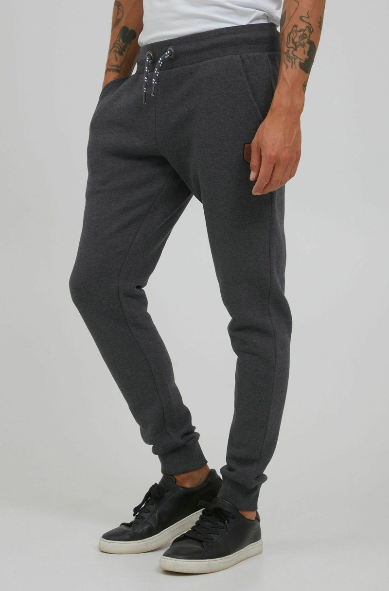 Los pantalones de chándal gris oscuro cuentan con una cintura elástica con cordones, bolsillos laterales y puños acanalados, fabricados con un material suave y texturizado.