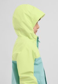 Chaqueta colorida con capucha amarilla y cuerpo turquesa. Fabricada con un material liso y resistente al agua. Cuenta con un cierre de cremallera y capucha con goma.