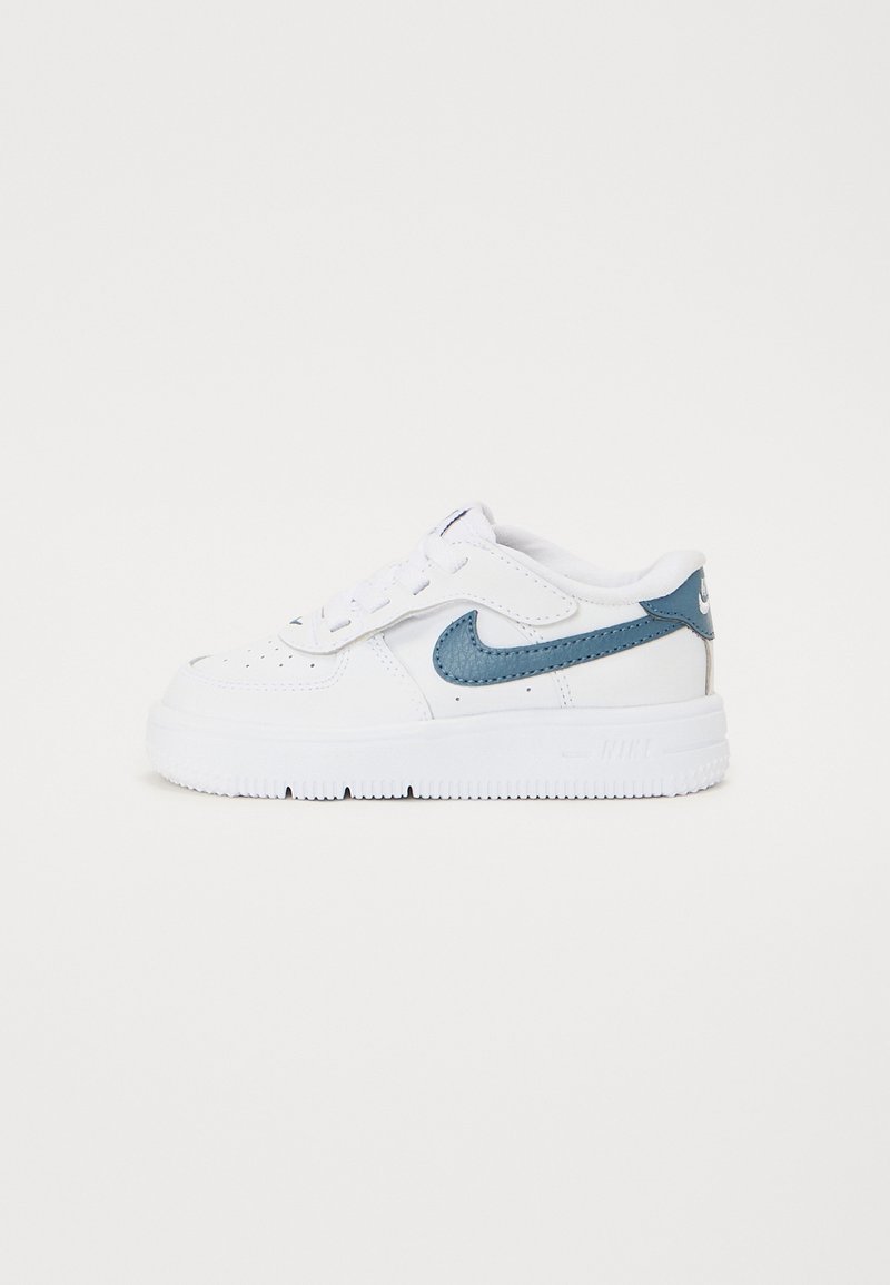 Valkoinen Nike-tenniskenkä, jossa on teksturoidut teal-väriset swooshit, sileä nahkapinta, matala profiili ja kumipohja. Varusteena nauhat ja rei'itetty kärki hengittävyyttä varten.
