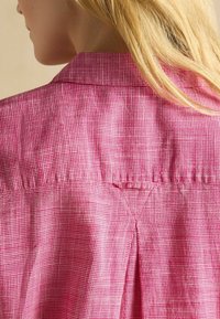 Ružová károvaná košeľa s chrbtovým záhybom a golierom, vyrobená z textúrovanej látky, ktorá zvýrazňuje vizuálnu hĺbku a vzor.
